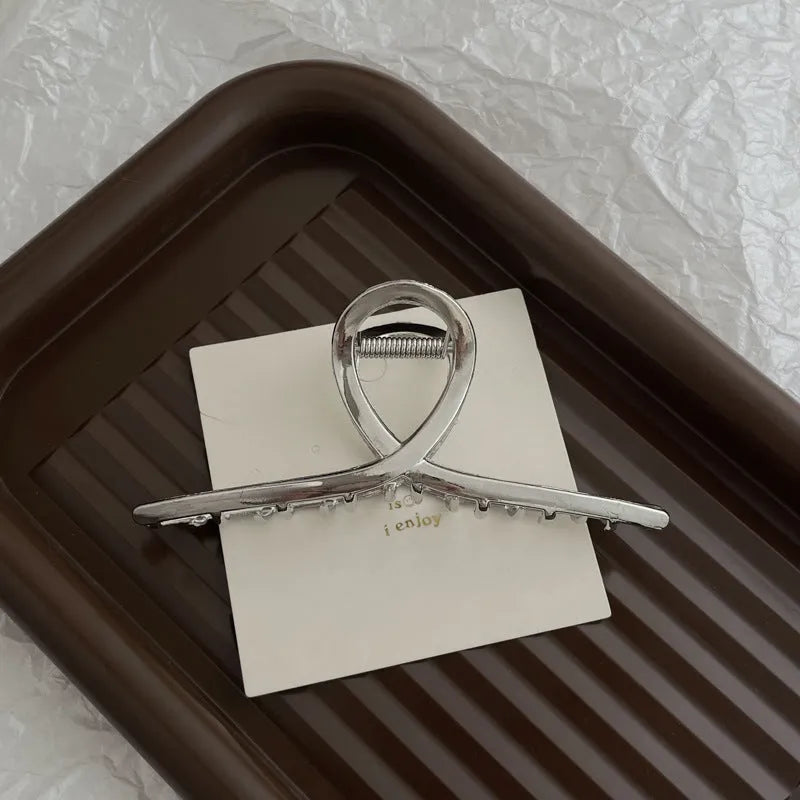 Silver metal hair claw clip assortment showing bows, waves, pearl designs, and geometric shapes from 4cm to 13.5cm