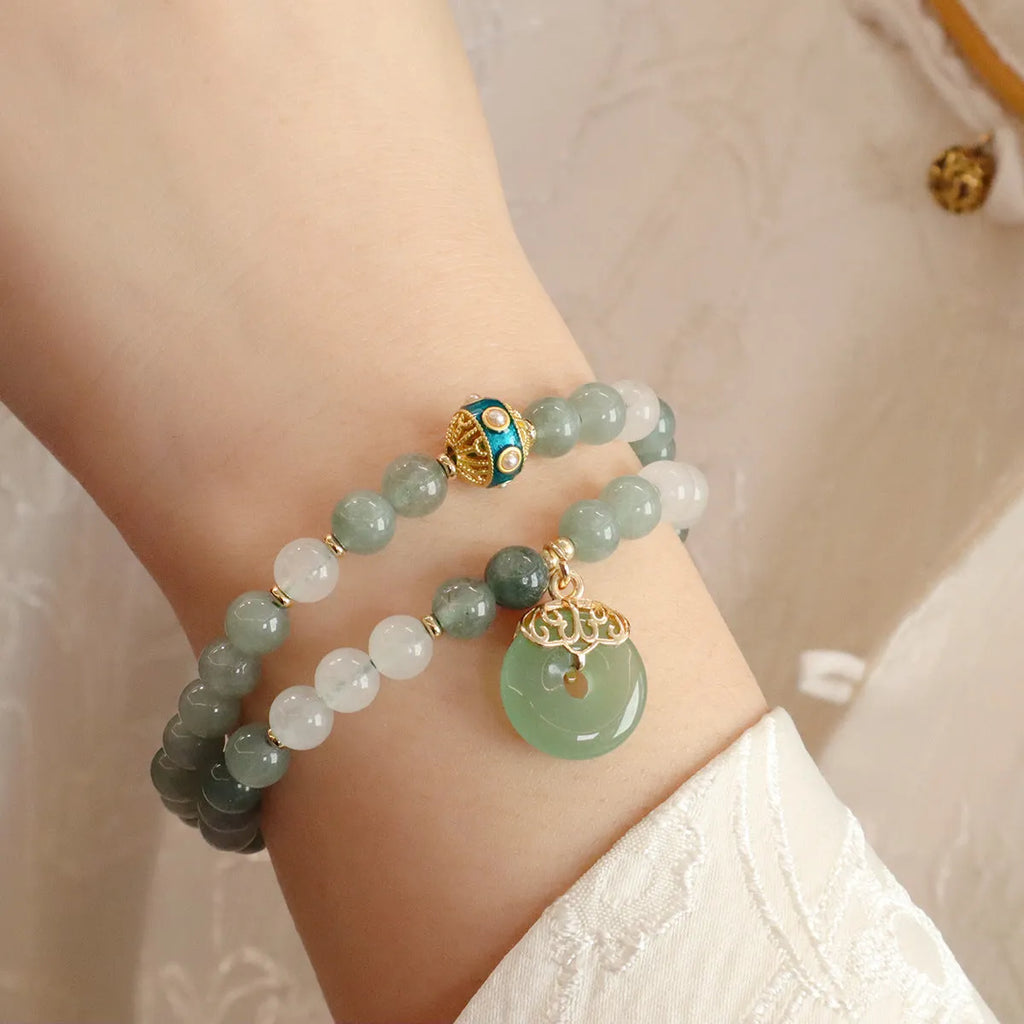 Close-up of a women's Myanmar jade bracelet with a silver geometric safety buckle pendant and lucky bead charms.