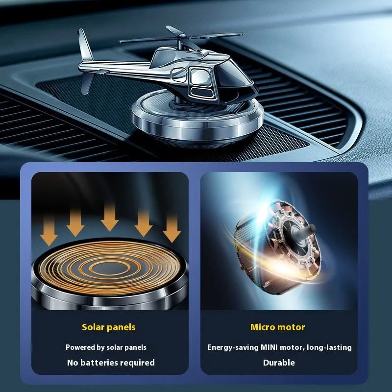 Silver metal solar helicopter car air freshener ornament with rotating blades on a car dashboard.