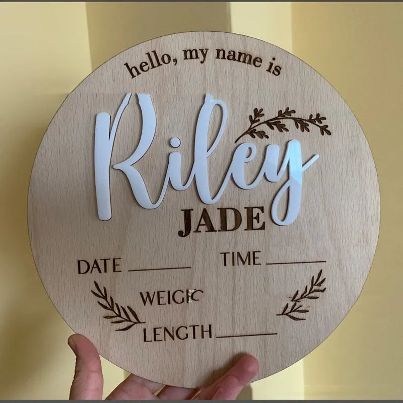 Square wooden newborn name label showing baby birth information and surname on a plywood plaque.