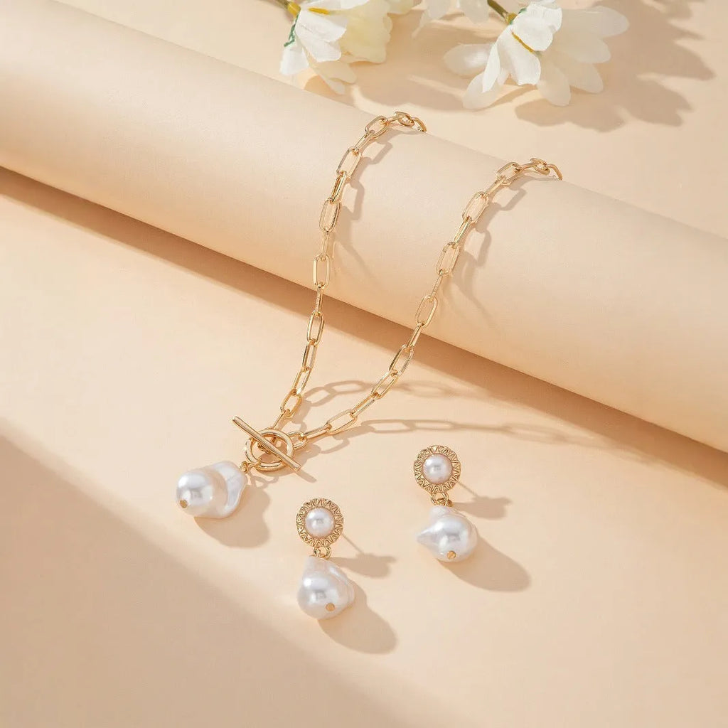 Gold-coloured retro baroque pearl pendant necklace and matching stud earrings set on a dark background.