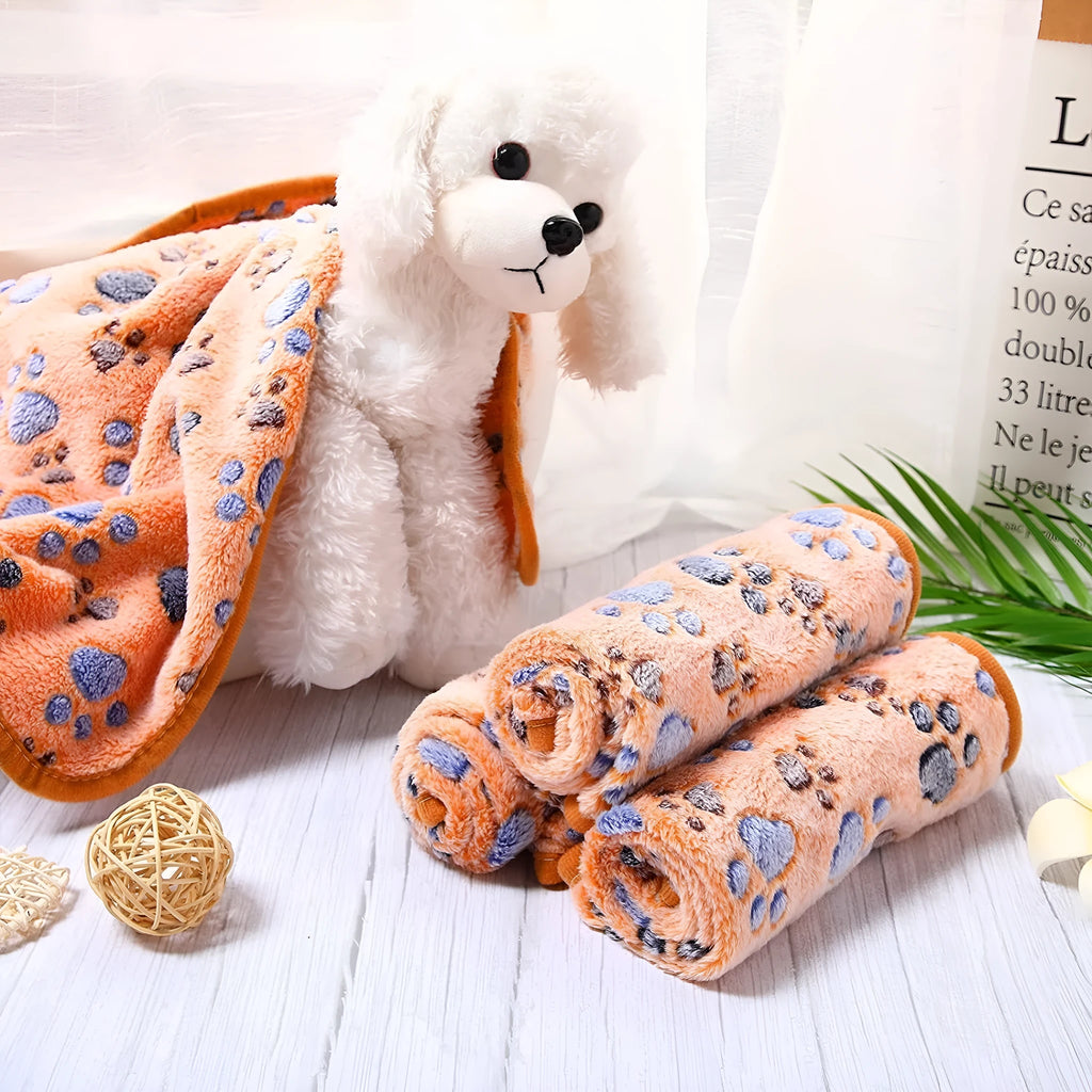 Coral fleece pet blanket with dog's paw print pattern in beige, shown in a large size on a dog bed.