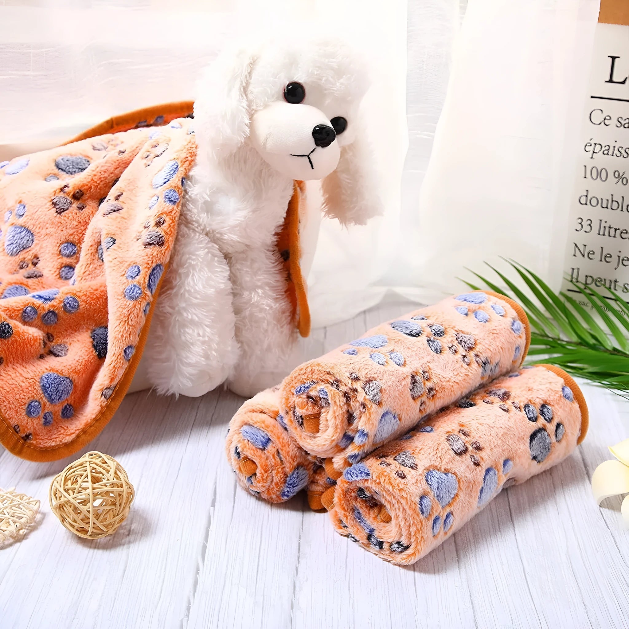 Coral fleece pet blanket with dog's paw print pattern in beige, shown in a large size on a dog bed.