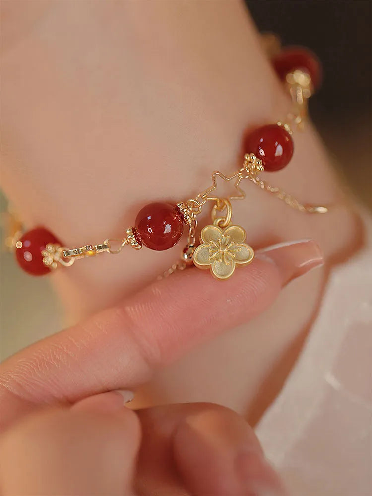 Red agate double layer bracelet with floral and peach blossom charms on a wrist.