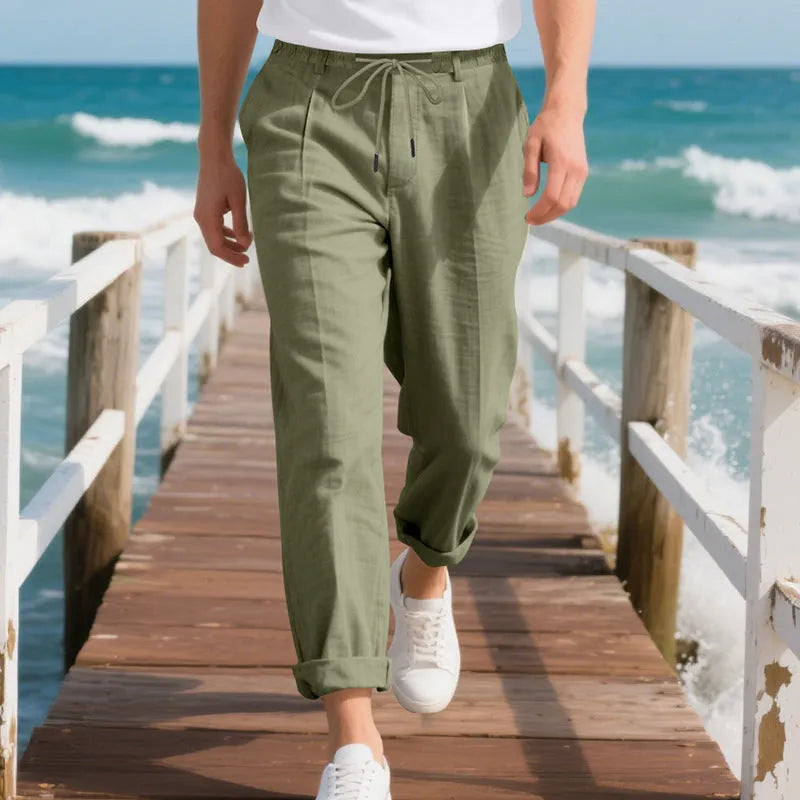 Men's straight leg linen trousers in light khaki colour with drawstring waist, laid flat.