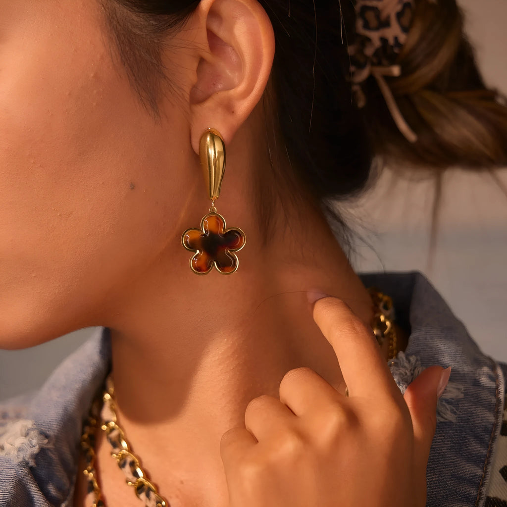 A pair of gold-coloured geometric earrings with a heart shape and a floral design on a white background.