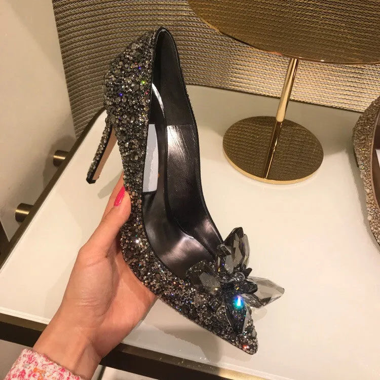 Gold women's pointed toe stiletto heels with rhinestone and bow decoration on a sequin cloth upper.
