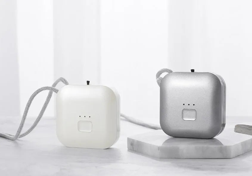 Small pink USB portable air purifier necklace on a table with charging cable.