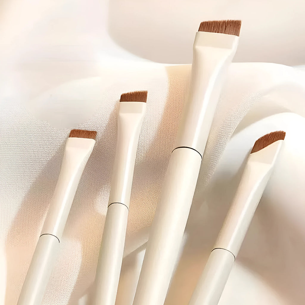 Four angled eyeliner and eyebrow makeup brushes stored in a brown leather case.