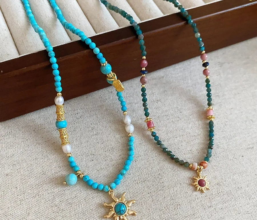French royal style sun necklace with freshwater pearls and a blue stone geometry pendant on a gold chain.
