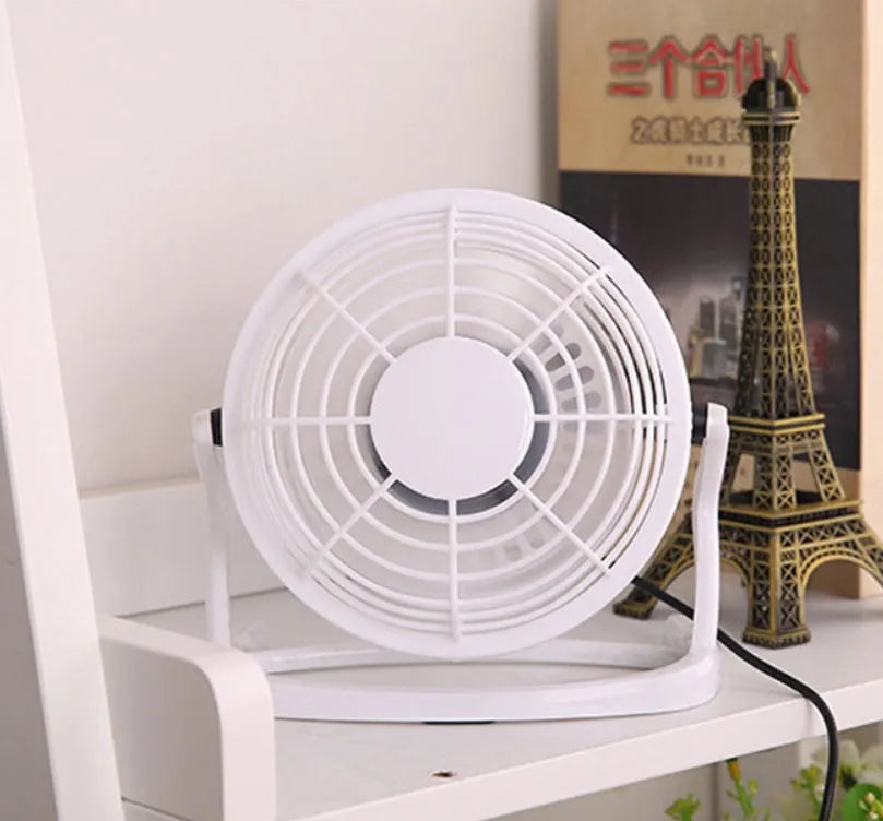 Black mini USB desk fan with adjustable head on a wooden desk next to a laptop.