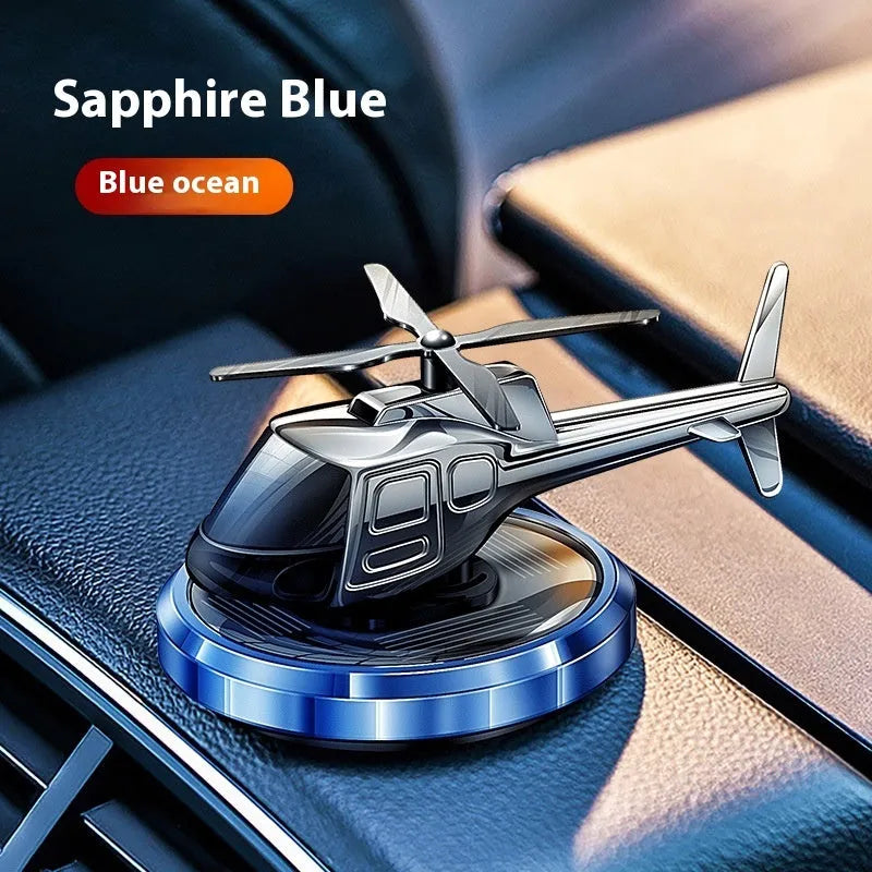 Silver metal solar helicopter car air freshener ornament with rotating blades on a car dashboard.