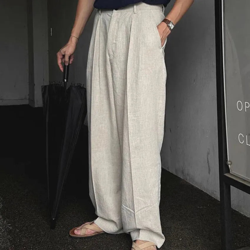 Man wearing apricot coloured loose wide-leg cotton linen trousers with a pencil leg opening.