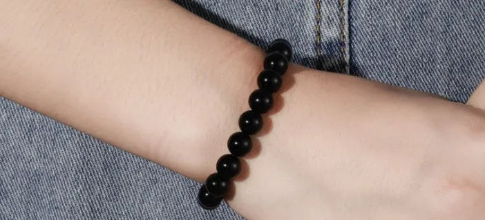 Close-up of a women's black onyx agate bracelet with 8mm geometric beads on a black elastic cord.