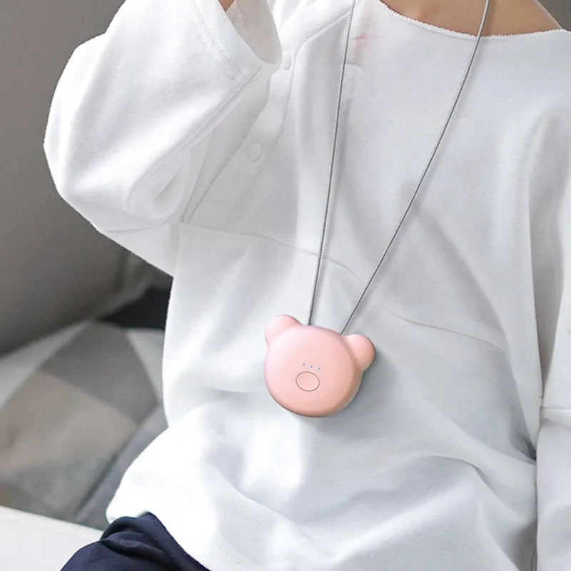 Small pink USB portable air purifier necklace on a table with charging cable.
