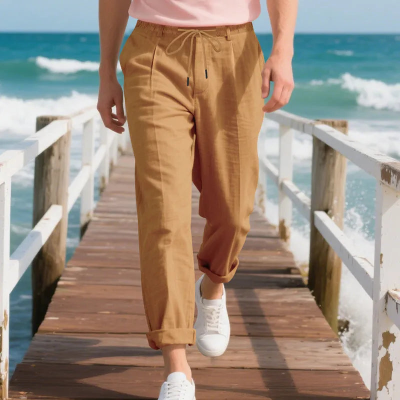 Men's straight leg linen trousers in light khaki colour with drawstring waist, laid flat.