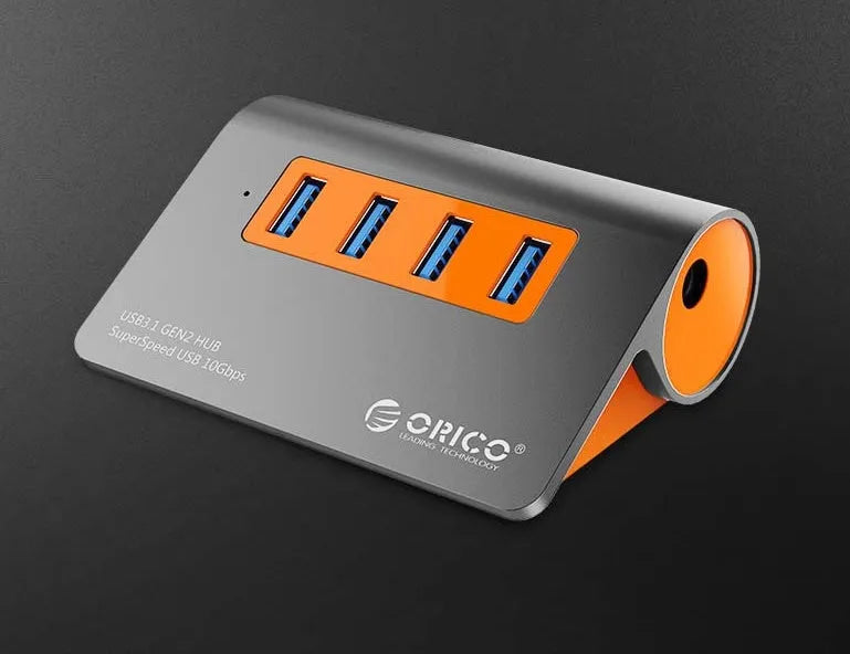 Dark grey aluminium USB-C docking station with four USB ports and orange accent, shown with a detached cable.