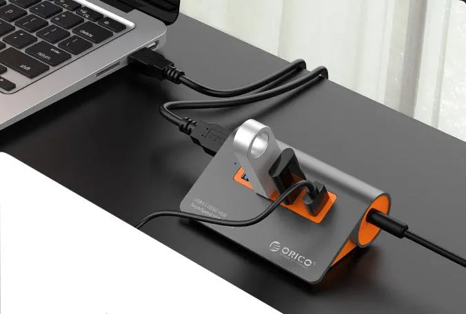 Dark grey aluminium USB-C docking station with four USB ports and orange accent, shown with a detached cable.