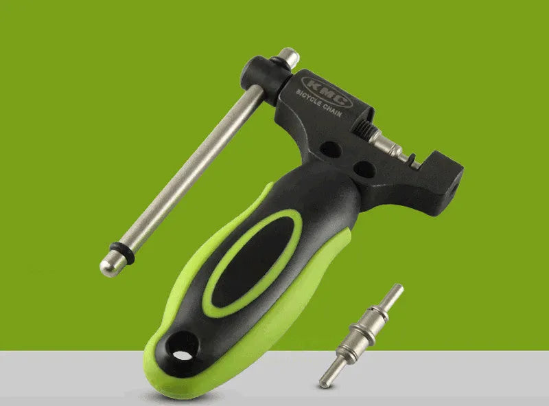 A green steel bicycle chain next to a double shaft chain cutting tool on a workshop surface.