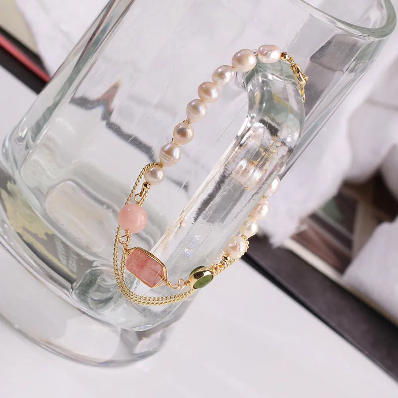 Close-up of a women's bracelet with geometric freshwater pearls and red strawberry crystal charms on a pink background.