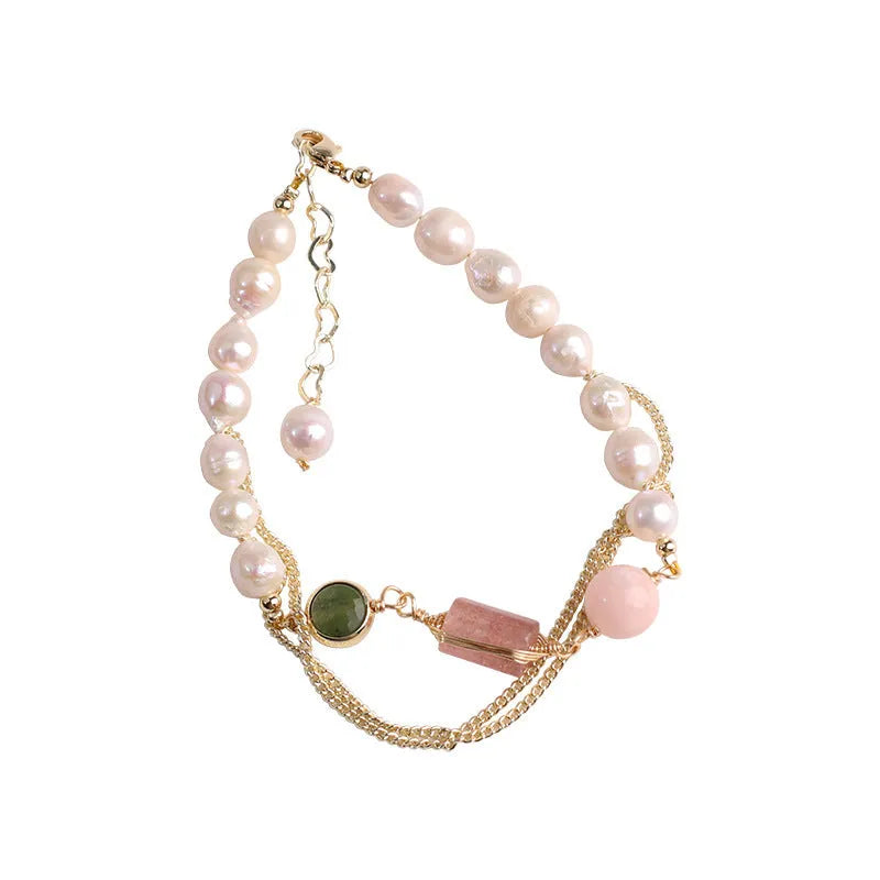 Close-up of a women's bracelet with geometric freshwater pearls and red strawberry crystal charms on a pink background.
