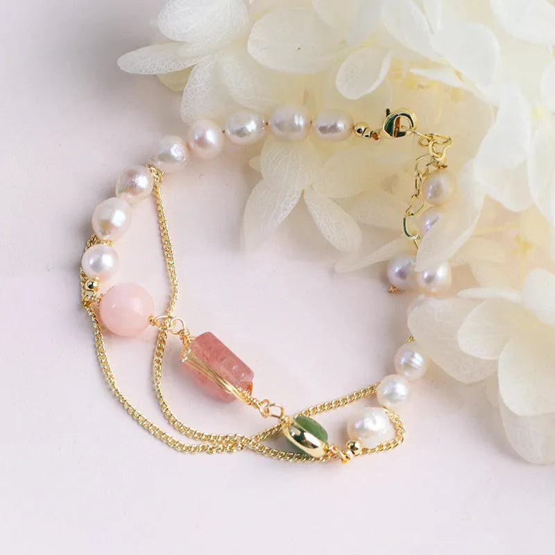 Close-up of a women's bracelet with geometric freshwater pearls and red strawberry crystal charms on a pink background.