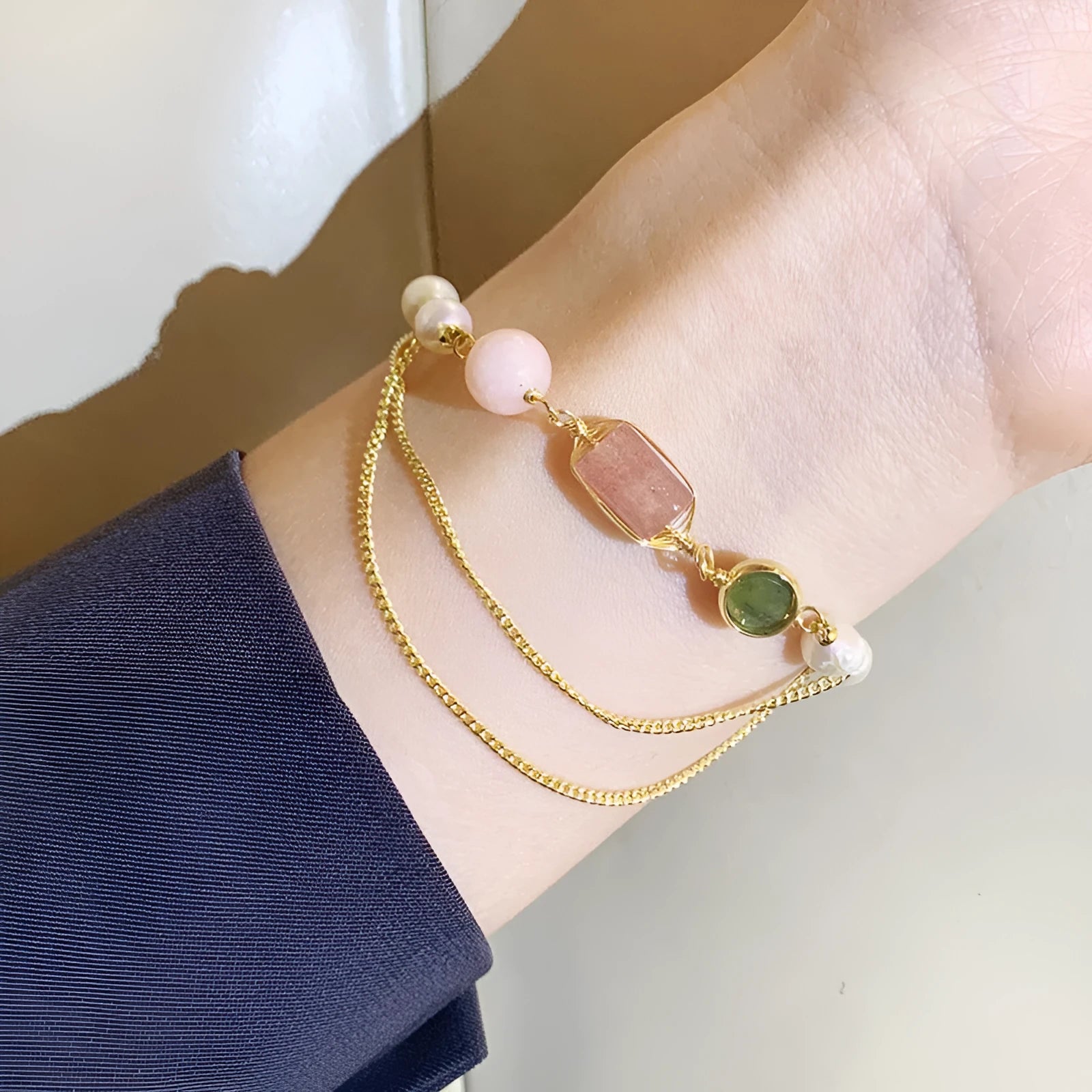 Close-up of a women's bracelet with geometric freshwater pearls and red strawberry crystal charms on a pink background.