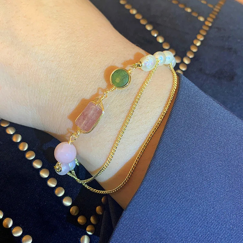 Close-up of a women's bracelet with geometric freshwater pearls and red strawberry crystal charms on a pink background.