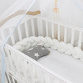Bendable braid-knot baby crib bumper in spandex velvet, shown in a light grey colour wrapped around a cot.