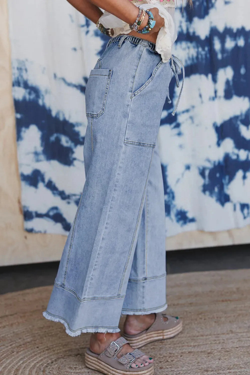 Beau blue wide leg denim trousers with a drawstring waist and raw hem on a hanger