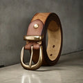 Men's black cattlehide leather belt with a copper pin buckle on a jeans background.