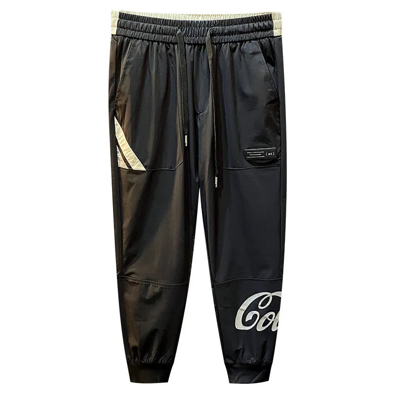 Black men's cropped casual trousers with an ankle-band cuff, laid flat to show the slim fit and cotton blend fabric.