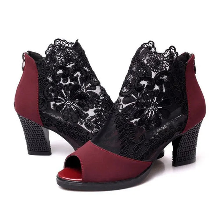 Black lace gladiator sandals with a flower motif, square high heel, and a front zip closure on a woman's foot.