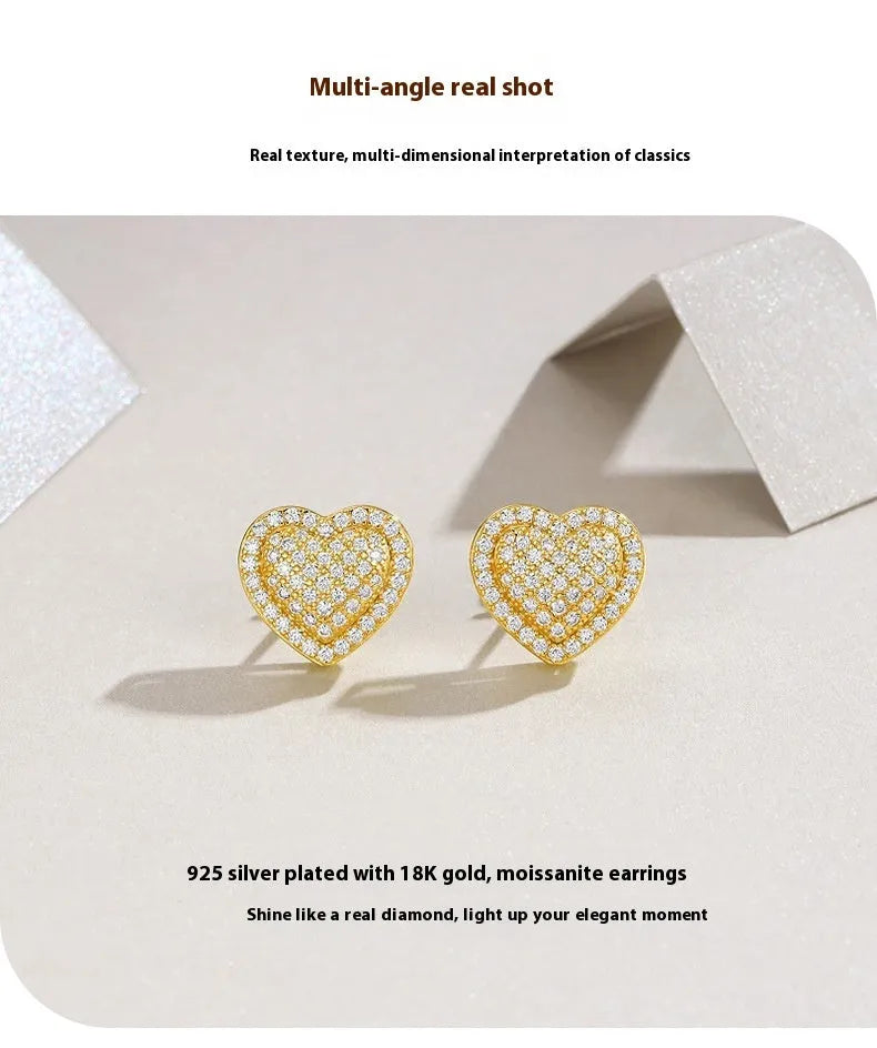 A pair of golden-colour heart stud earrings with a central moissanite stone, on a silver background.