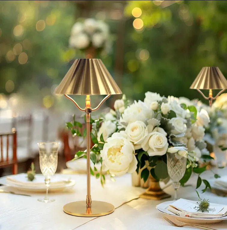 Gold-coloured alloy desk lamp with a cylindrical shade on a wooden desk.