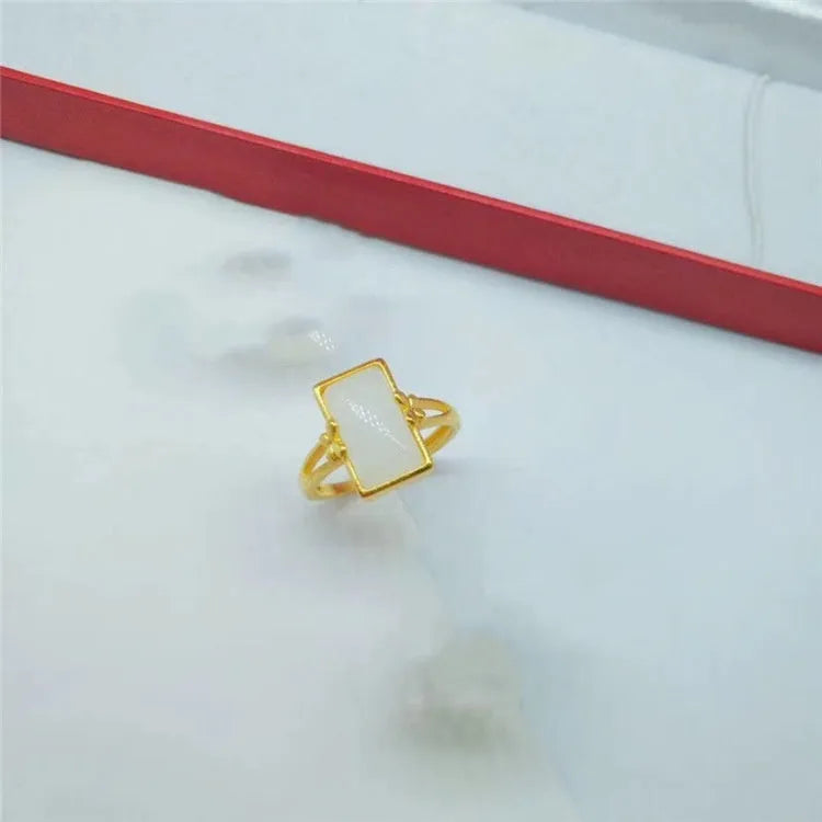 Adjustable brass gold-plated ring with a central green gemstone on a model's hand.