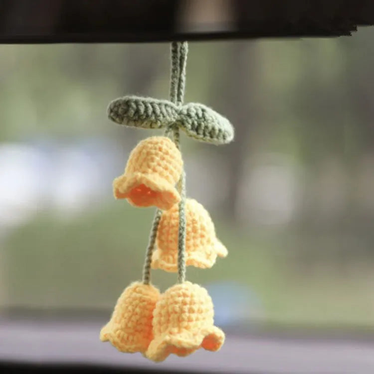 Green and white knitted wool car plant decoration with hanging rope on a car dashboard