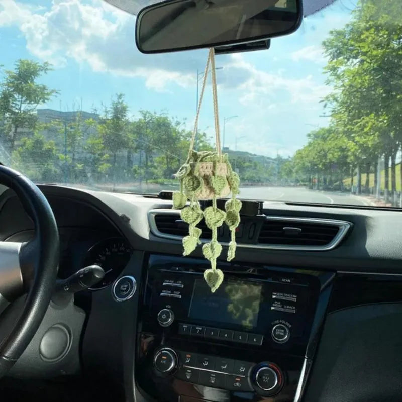 Green and white knitted wool car plant decoration with hanging rope on a car dashboard