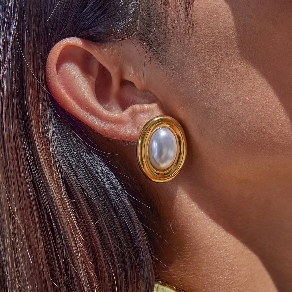 Small gold-tone stainless steel stud earrings with a white pearl accent on a grey background.