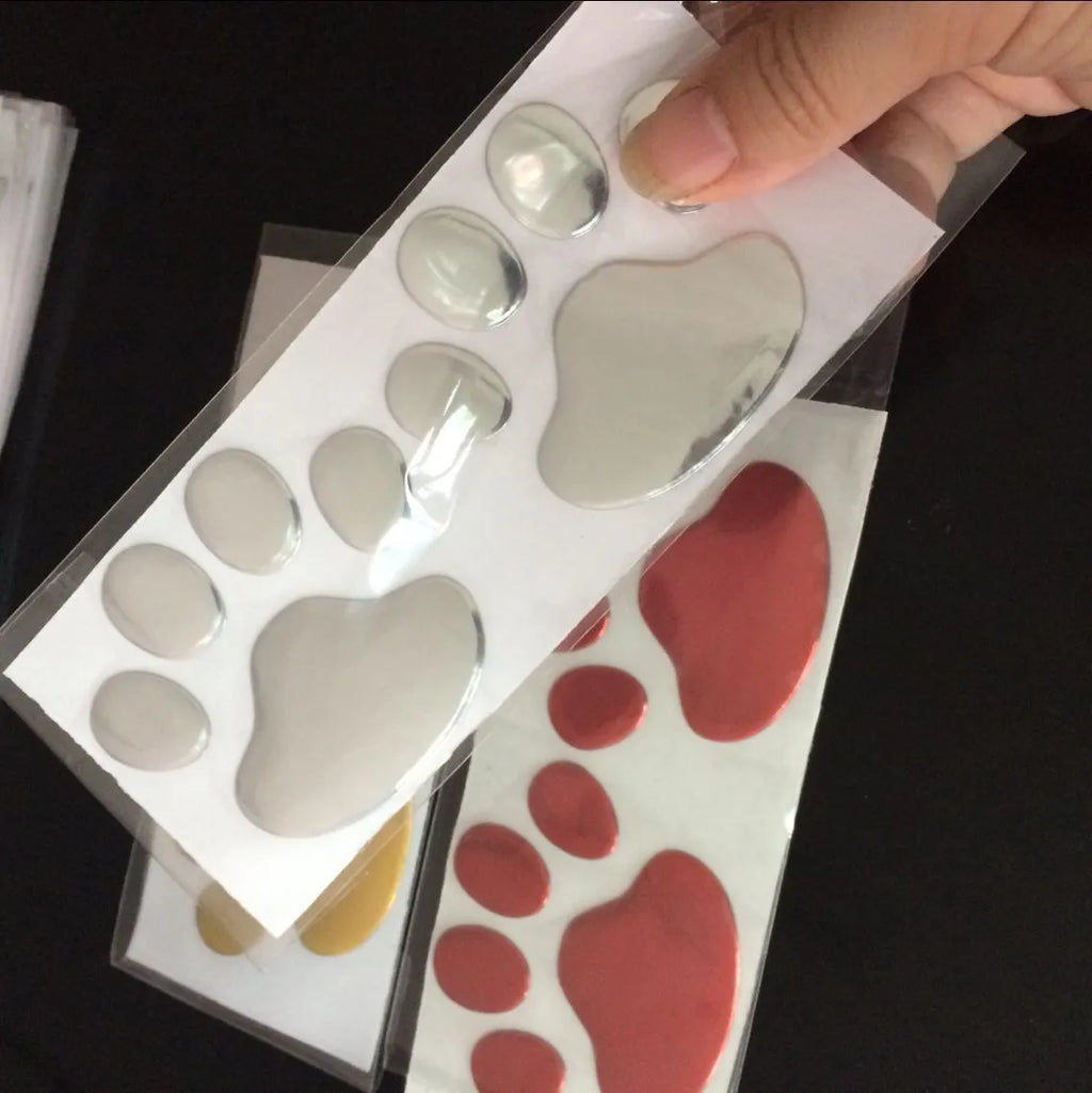 Pair of hand-shaped brush dog footprint PVC car stickers in red, shown against a car bumper.