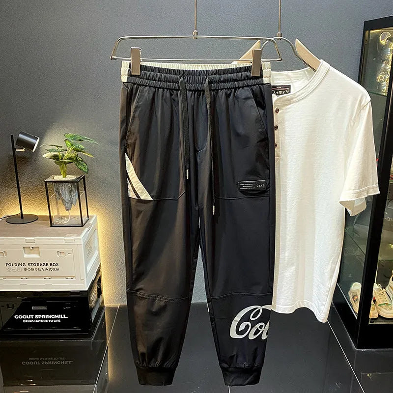 Black men's cropped casual trousers with an ankle-band cuff, laid flat to show the slim fit and cotton blend fabric.