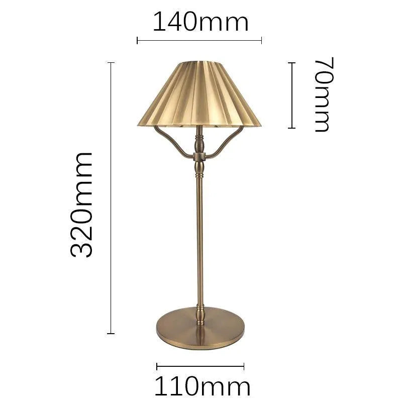 Gold-coloured alloy desk lamp with a cylindrical shade on a wooden desk.
