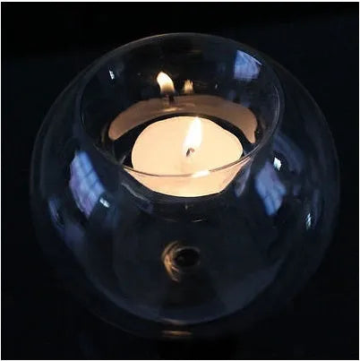 Handmade round hollow glass candle holder with openwork holes, shown on a table.