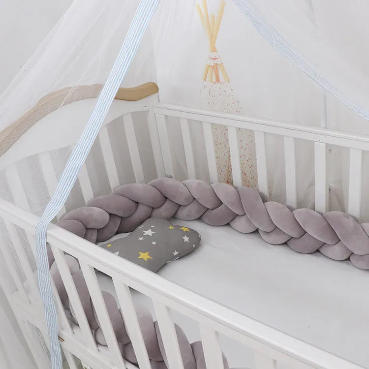 Bendable braid-knot baby crib bumper in spandex velvet, shown in a light grey colour wrapped around a cot.