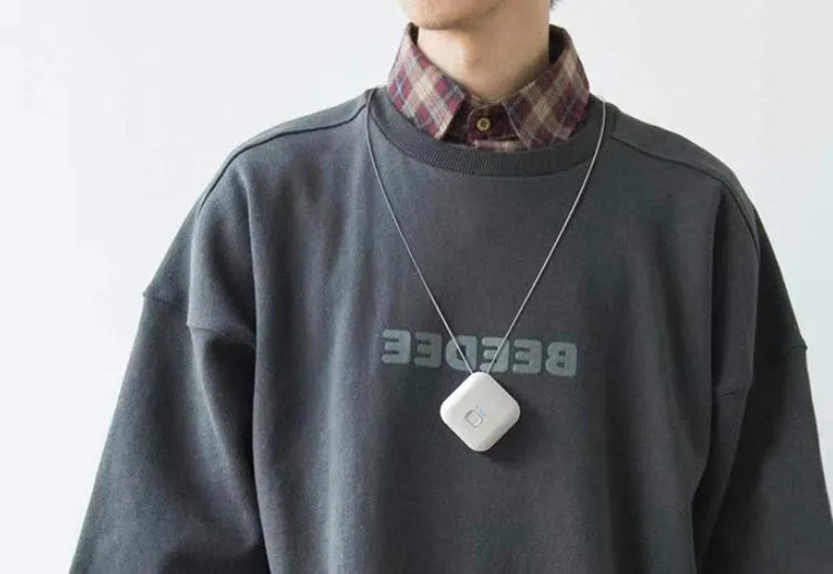 Small pink USB portable air purifier necklace on a table with charging cable.