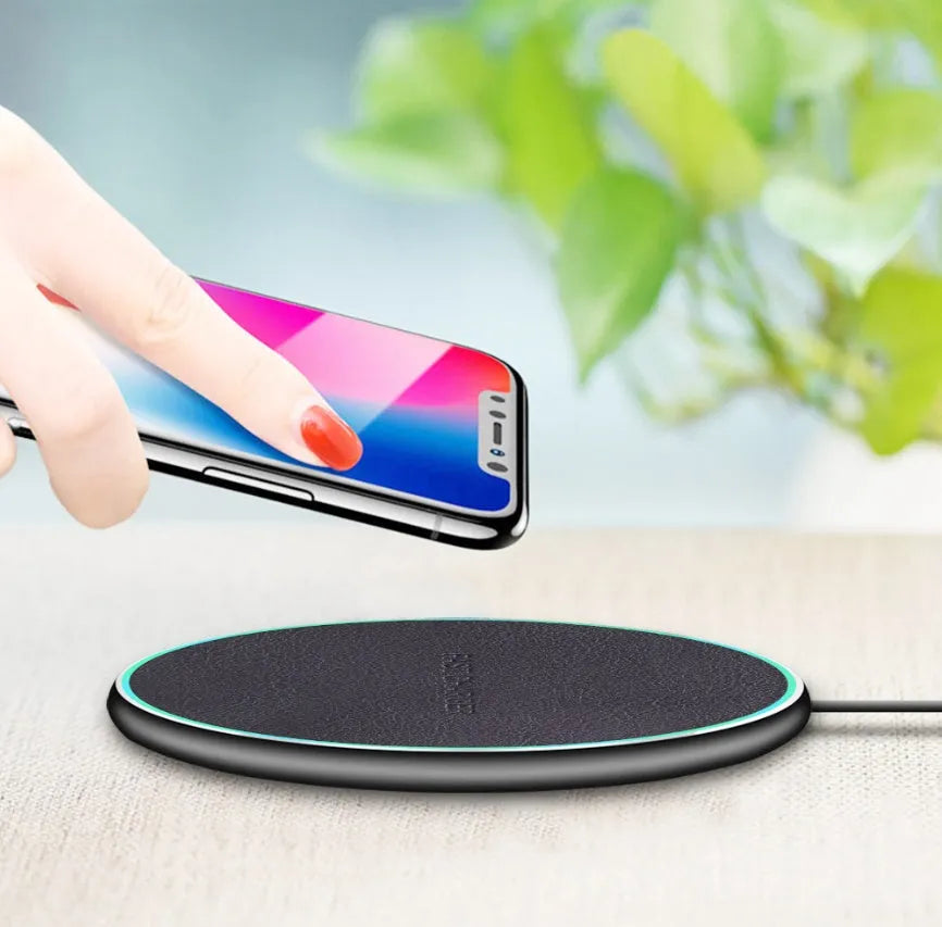 Black Qi wireless charging pad with built-in stand for iPhone 11 on a desk.