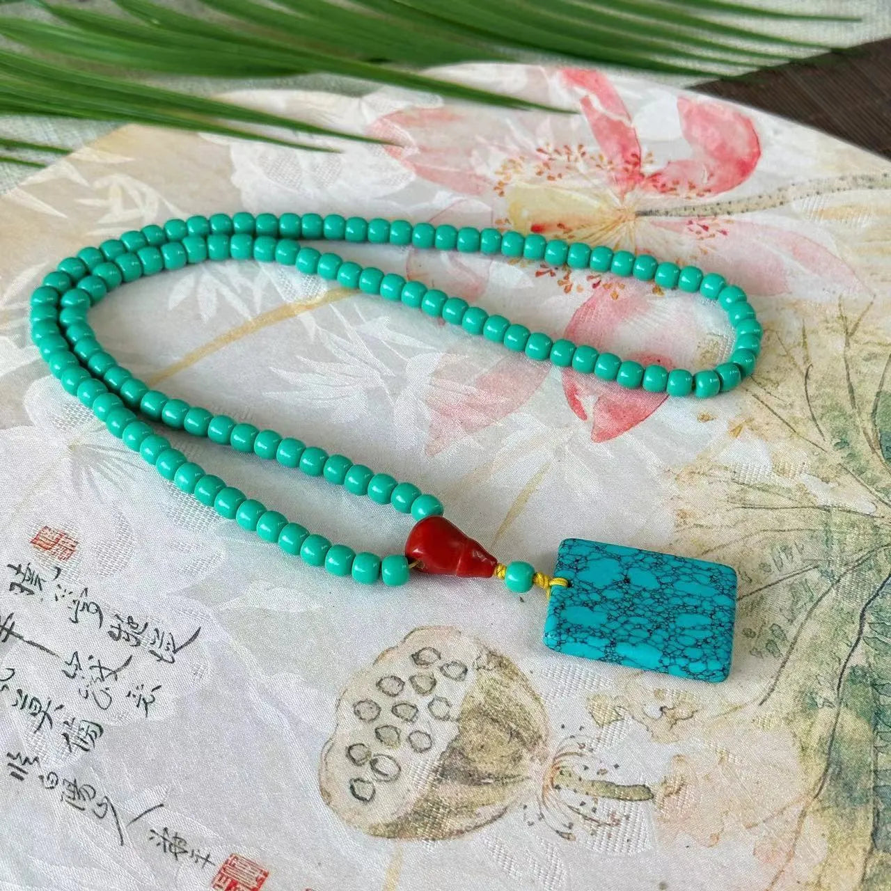 Turquoise stone pendant with hand-woven mesh flower design on a ball bead necklace chain.