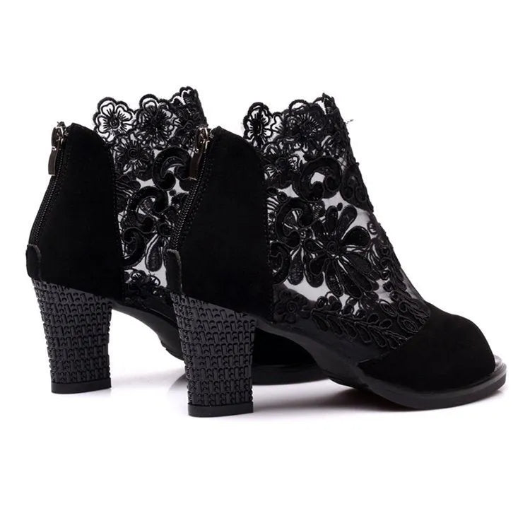 Black lace gladiator sandals with a flower motif, square high heel, and a front zip closure on a woman's foot.