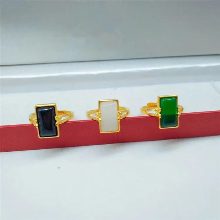 Adjustable brass gold-plated ring with a central green gemstone on a model's hand.