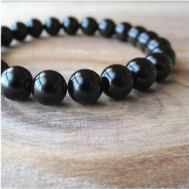 Close-up of a women's black onyx agate bracelet with 8mm geometric beads on a black elastic cord.